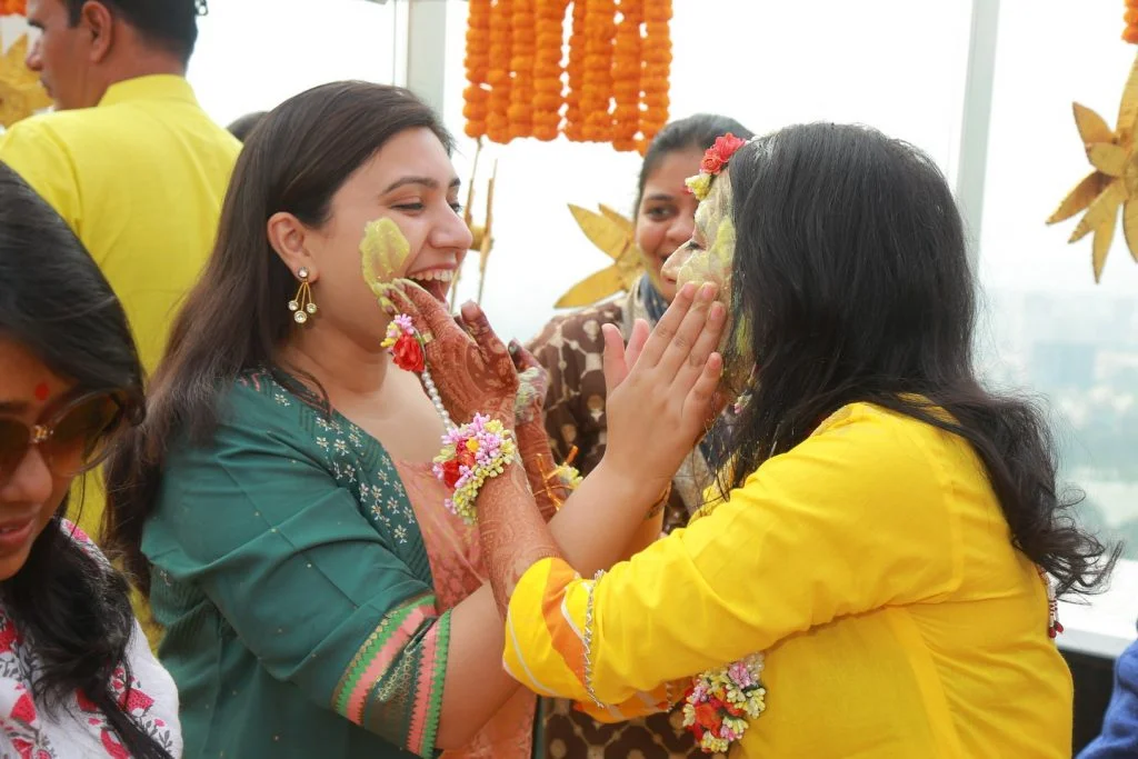 candid of bride applying mehendi to bridesmaid in haldi function