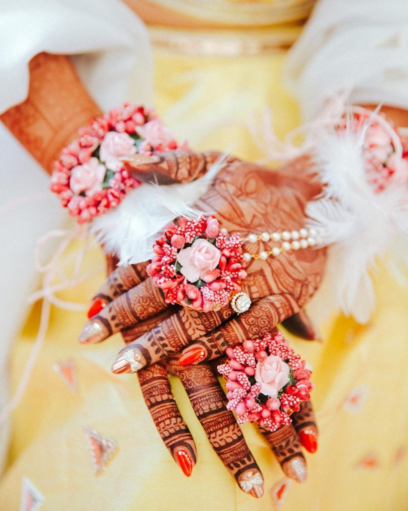 golden red bridal nail art with 3d bow embellishments and pink haldi flower jewelry