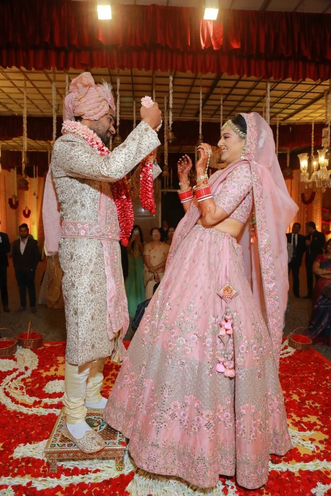 groom in white sherwani with bride in pink lehenga puting varmala
