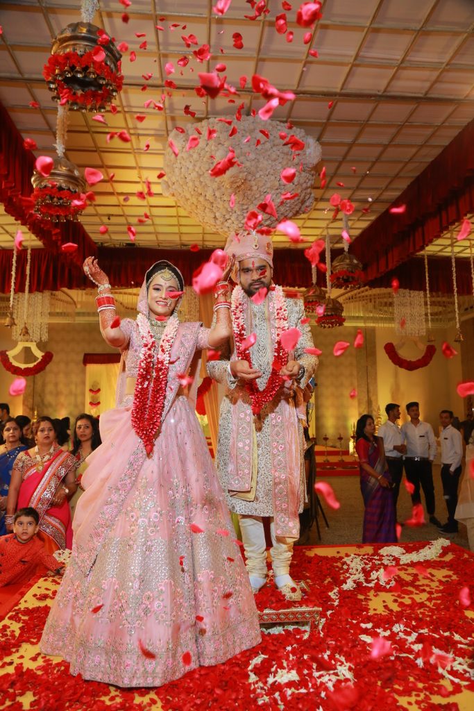 indian bride in read jaimala throwing roses at the camera with groom