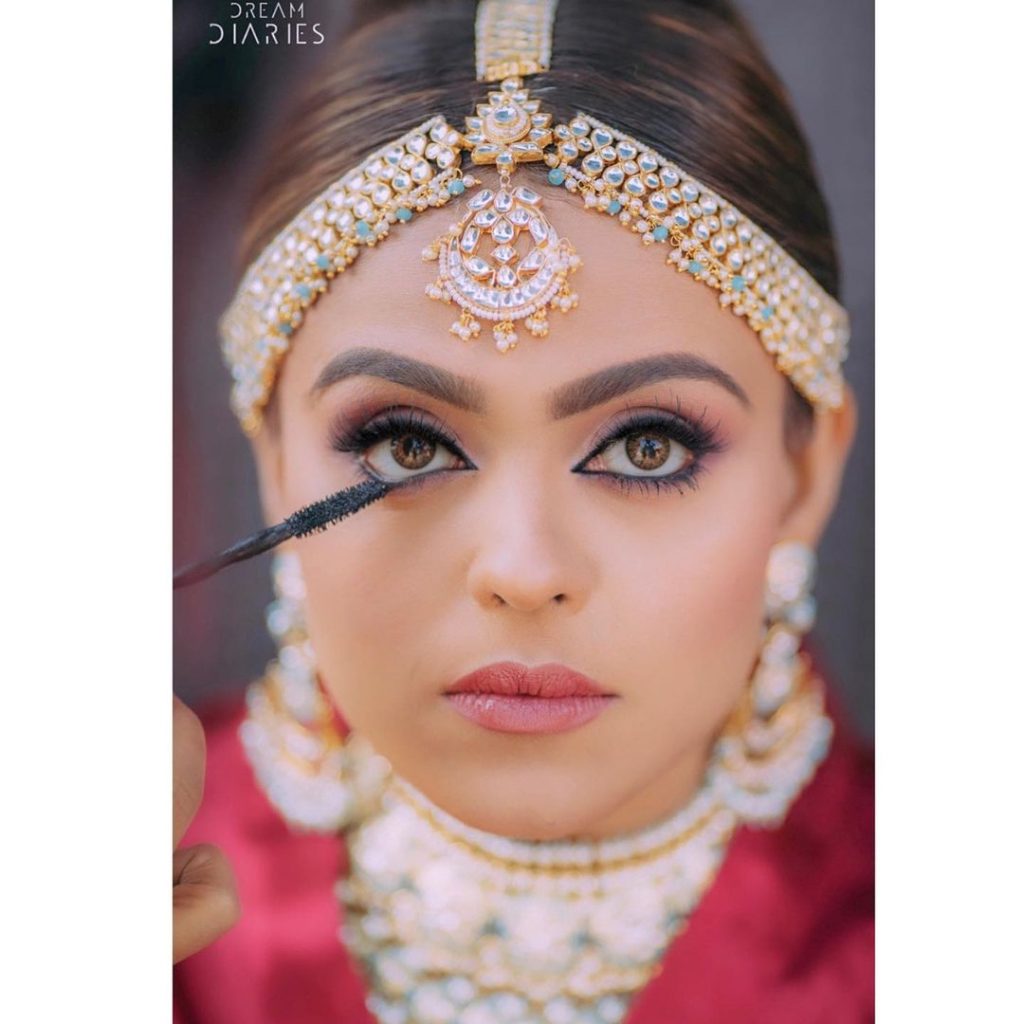 bride defining her eyelashes with mascara from her bridal makeup kit box