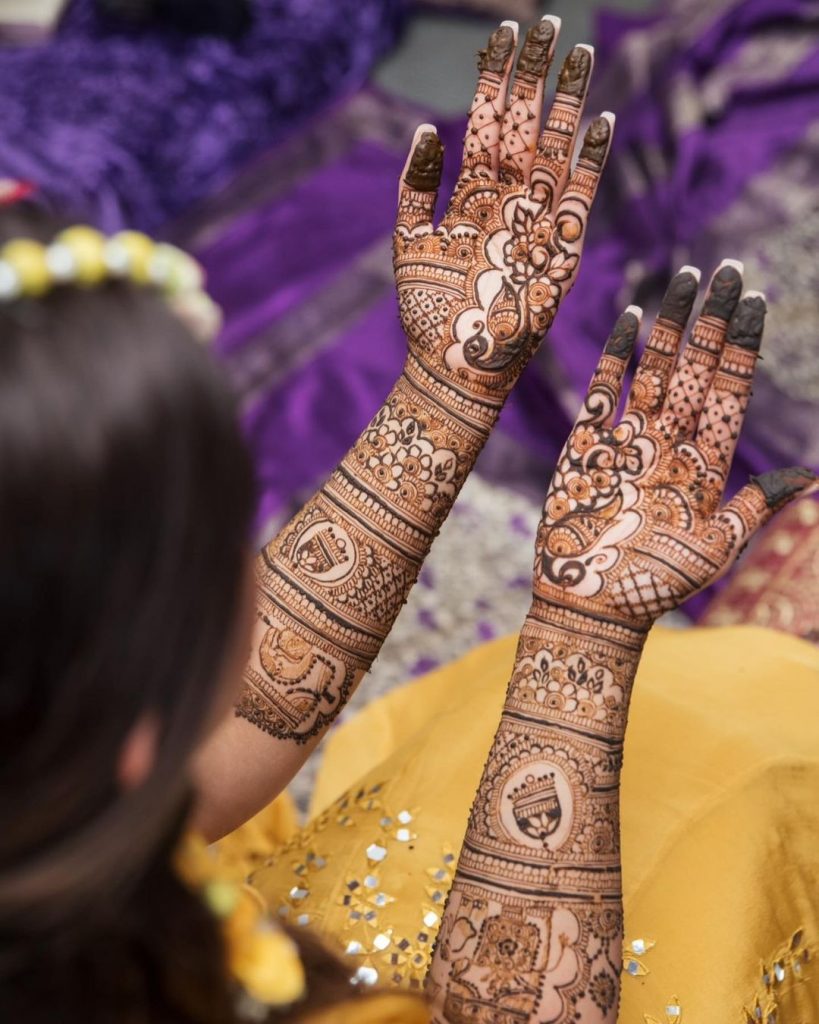 Intricate front hand bridal mehndi design with peacock and bell motifs