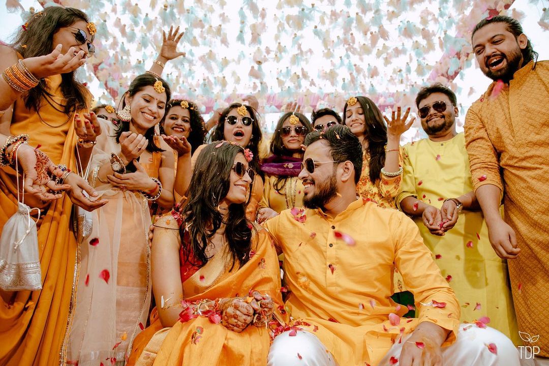 Photo of sisters and friends of the bride pose as the bride gets her  mehendi done